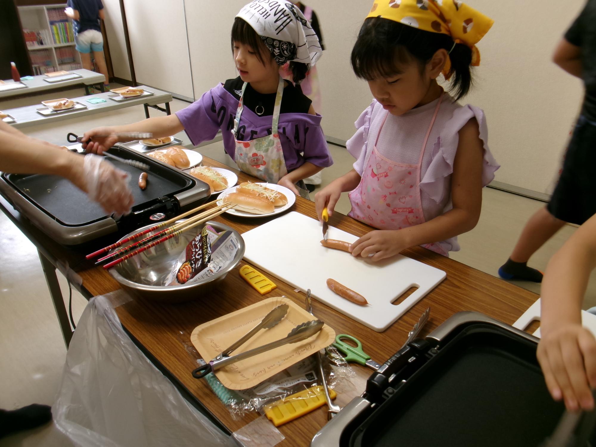 包丁でソーセージを切る小学生児童の様子の写真