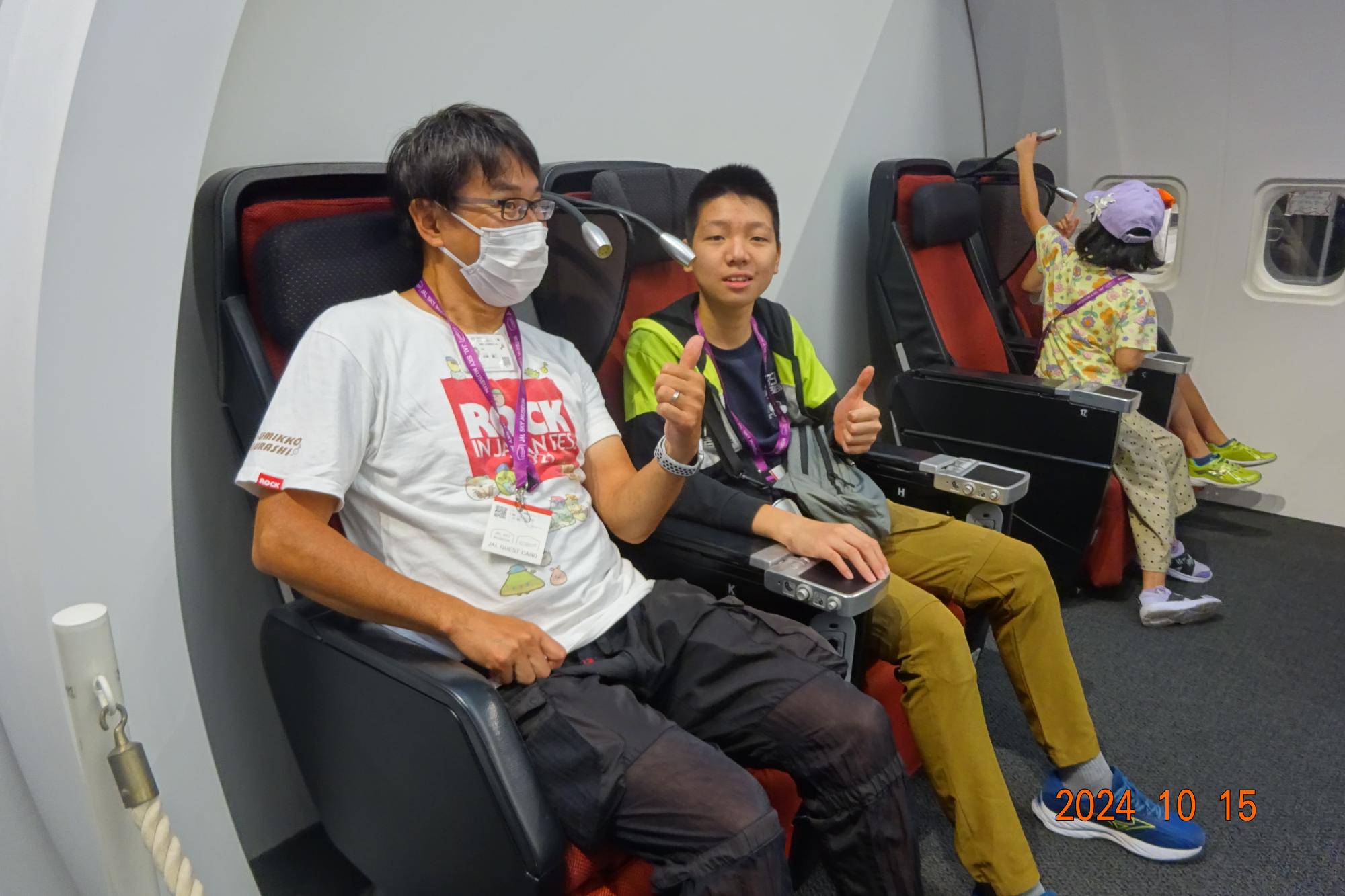 ファーストクラスの座席に座る体験をしている小学生児童と職員の写真