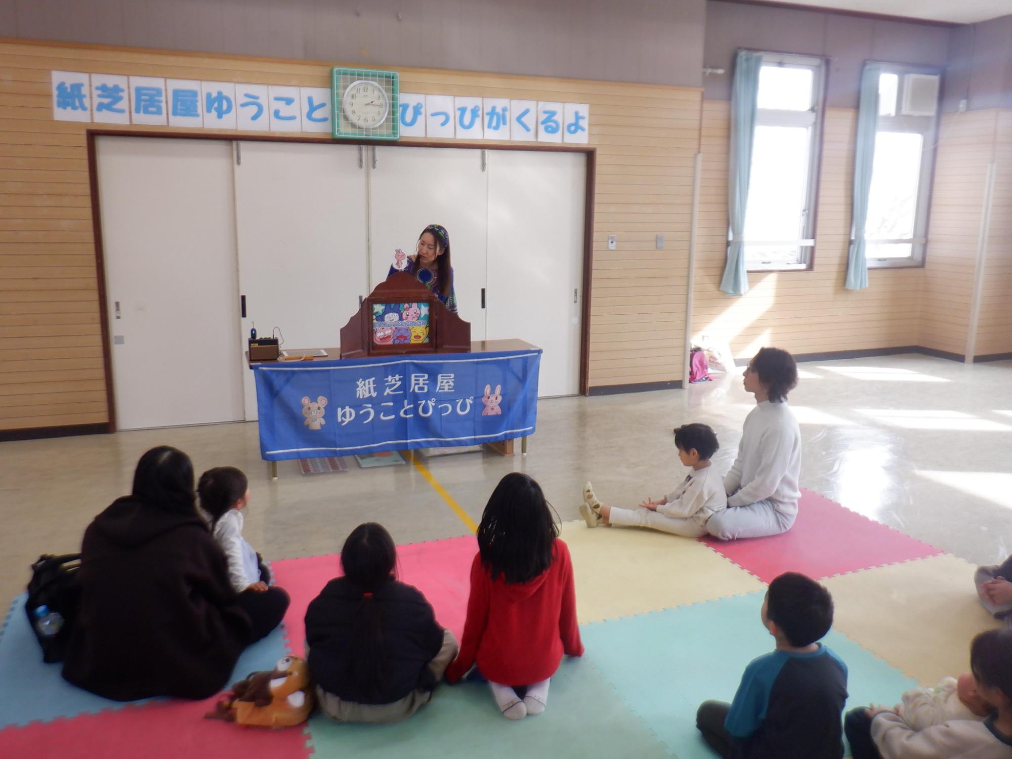 紙芝居を聞く乳幼児親子と小学生児童の写真