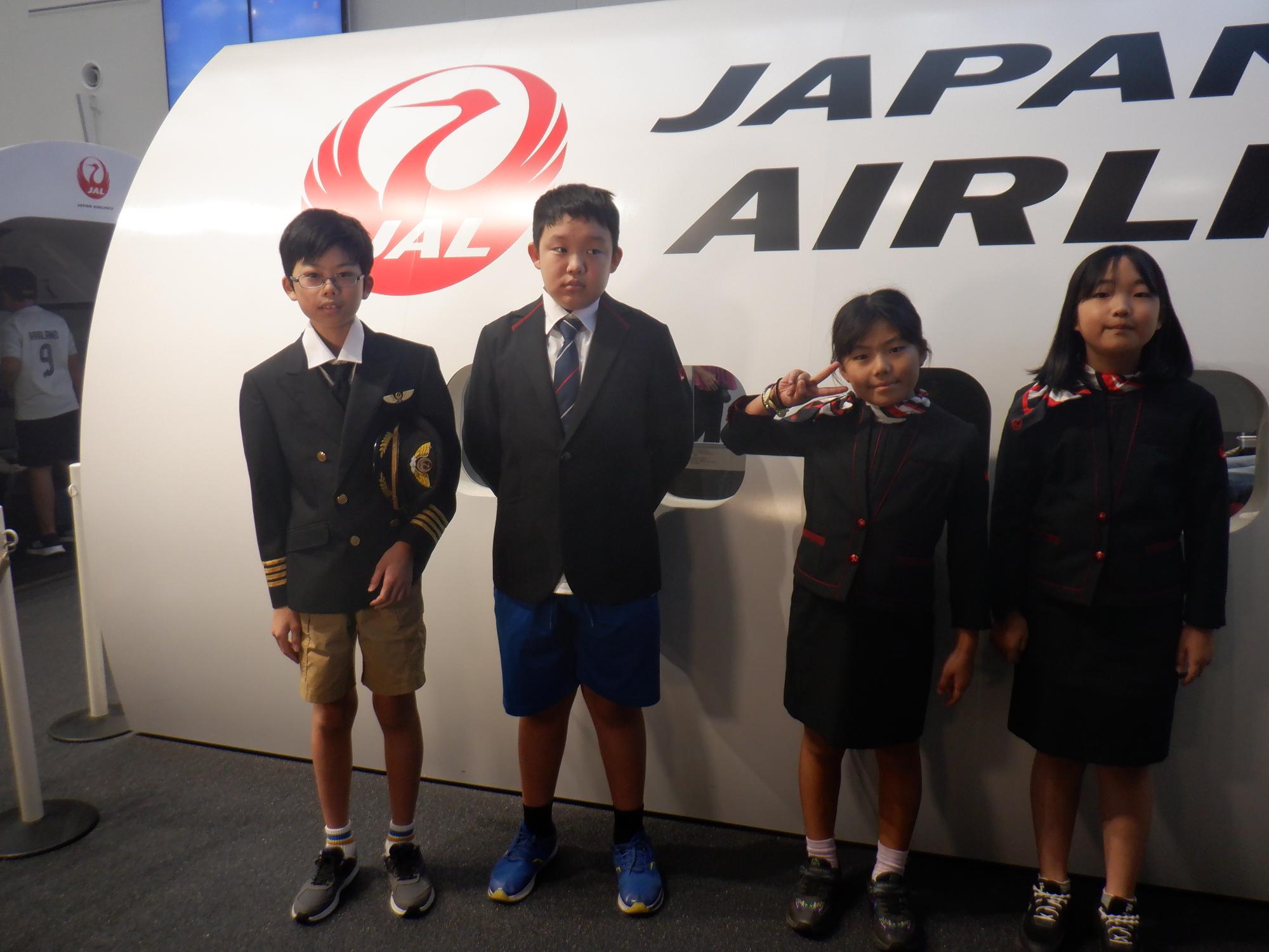 パイロットとCAスタッフの制服を着る体験をする小学生児童4名の写真