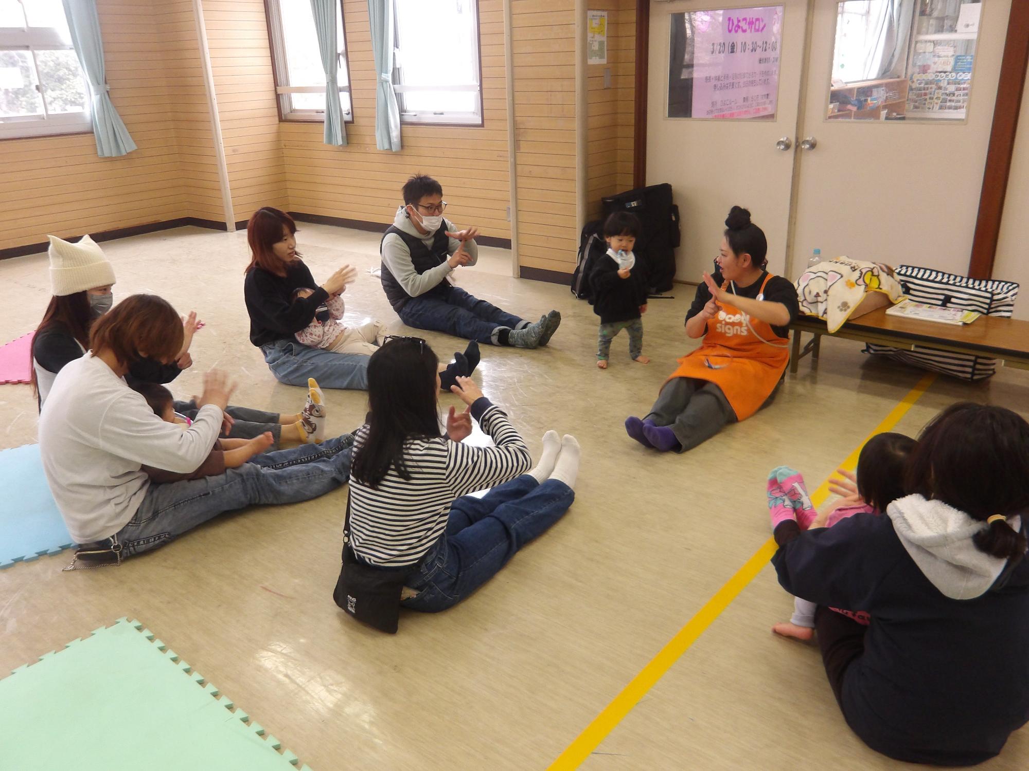 手作りおもちゃをハンドルに見立てて遊んでいる様子。お父さんやお母さんの膝に乗って、運転している。