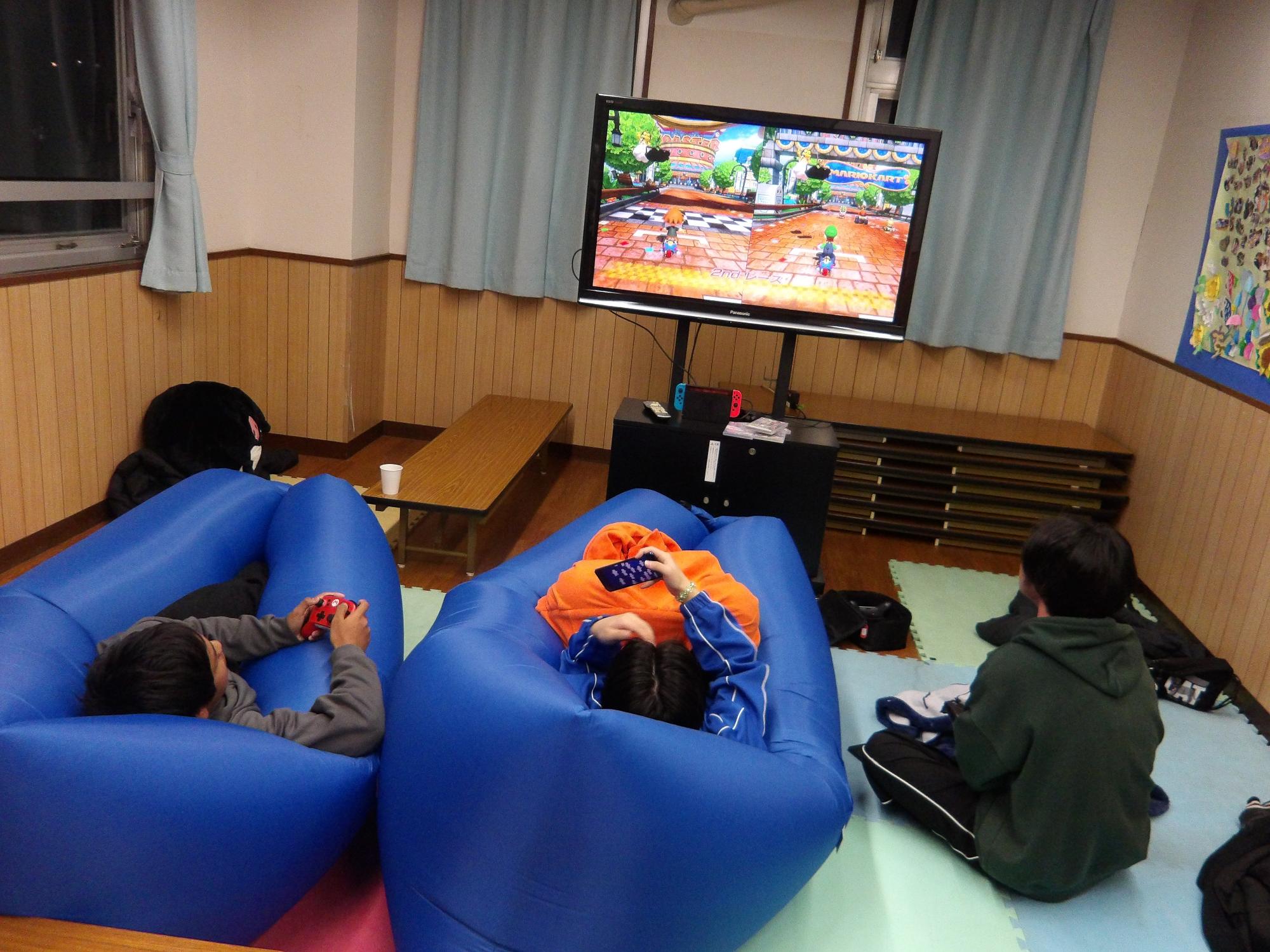 大きなエアークッションに寝そべったり、毛布をかけたりして、ゲームをする中高生の写真