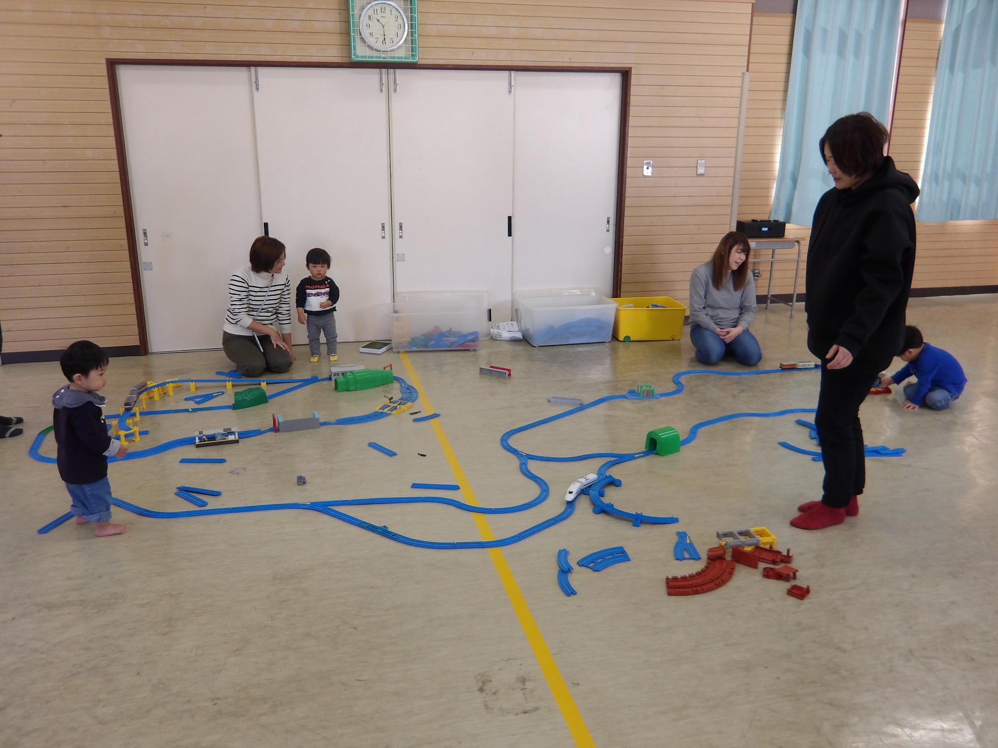大きな線路にプラ電車を走らせて遊ぶ親子の写真