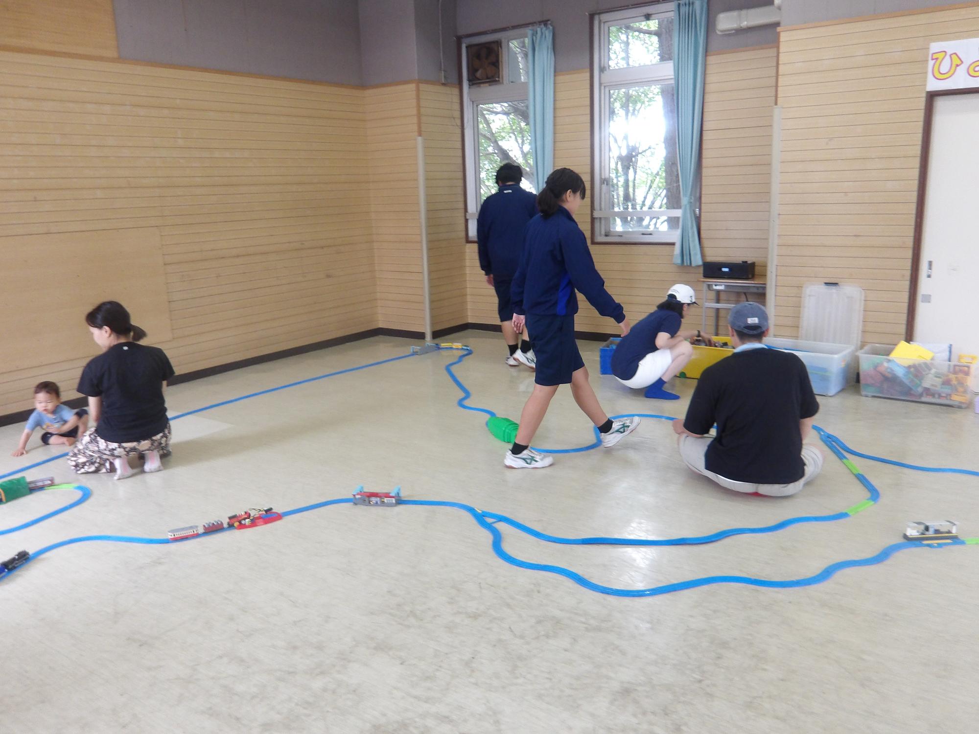 プラ電車を走らせている幼児と職場体験の中学生の様子