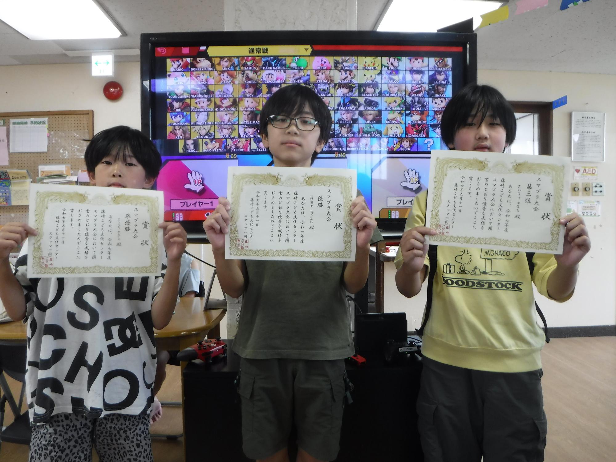 カーテンが閉められた部屋のフローリングの床の上に座ったり寝転んだりして、、プロジェクターを使って壁に映された映像を見ているたくさんの子どもたちの写真