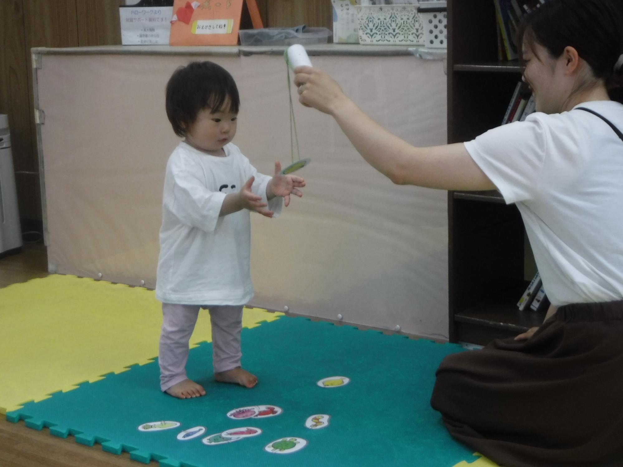 すまいるくらぶで魚釣り遊びをする幼児親子の写真