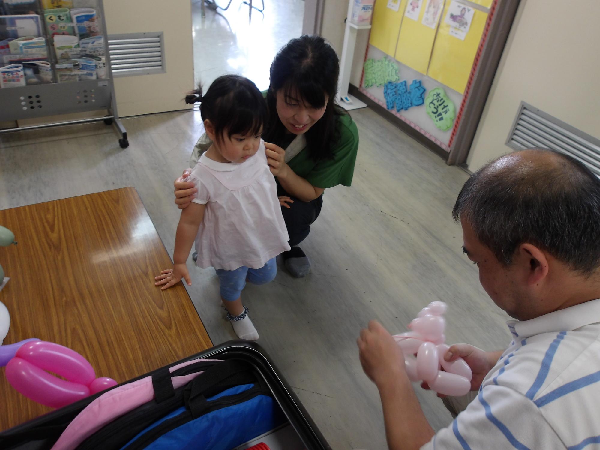 クマの風船を作ってもらっている幼児親子の様子