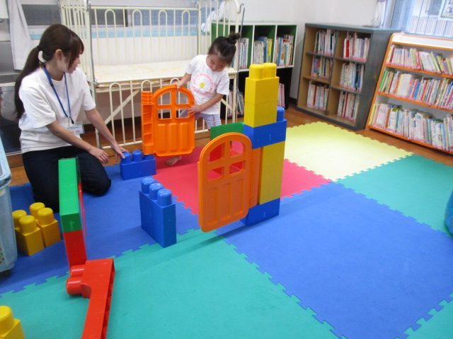 大型ブロックで遊んでいる幼児と職員の様子の写真