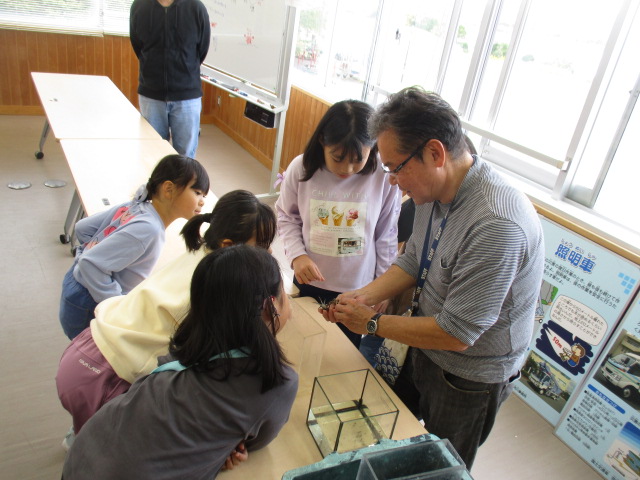 干潟で取ったカニを見ながら体の仕組みについての話を聞いている様子の写真