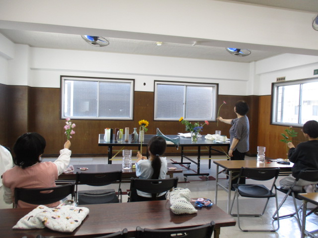 生花体験会の参加者が講師から花の生け方を教わっている様子の写真