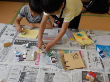 机が汚れないように新聞紙を敷いて作業をしている2人の子供たちの写真