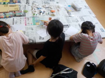 机に並んで黙々とカード作りをする3人の女の子の後ろ姿を撮った写真