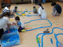 箱に入った沢山のパーツを取り出して組み立てる子供たちと見守る母親と父親の写真