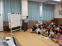 ビンゴ大会と書かれたホワイトボードを指さしている男性とそれをじっとみている子供たちの写真