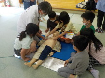 講師の方に手伝ってもらいながら、子供が人形にAEDのパットを貼り付けている写真
