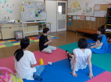 床に足を延ばして座り、子供を抱きながら女性講師の話を聞いている写真