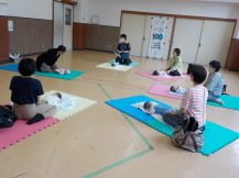 マッサージについて説明する講師の話を聞く参加者の乳幼児親子の写真