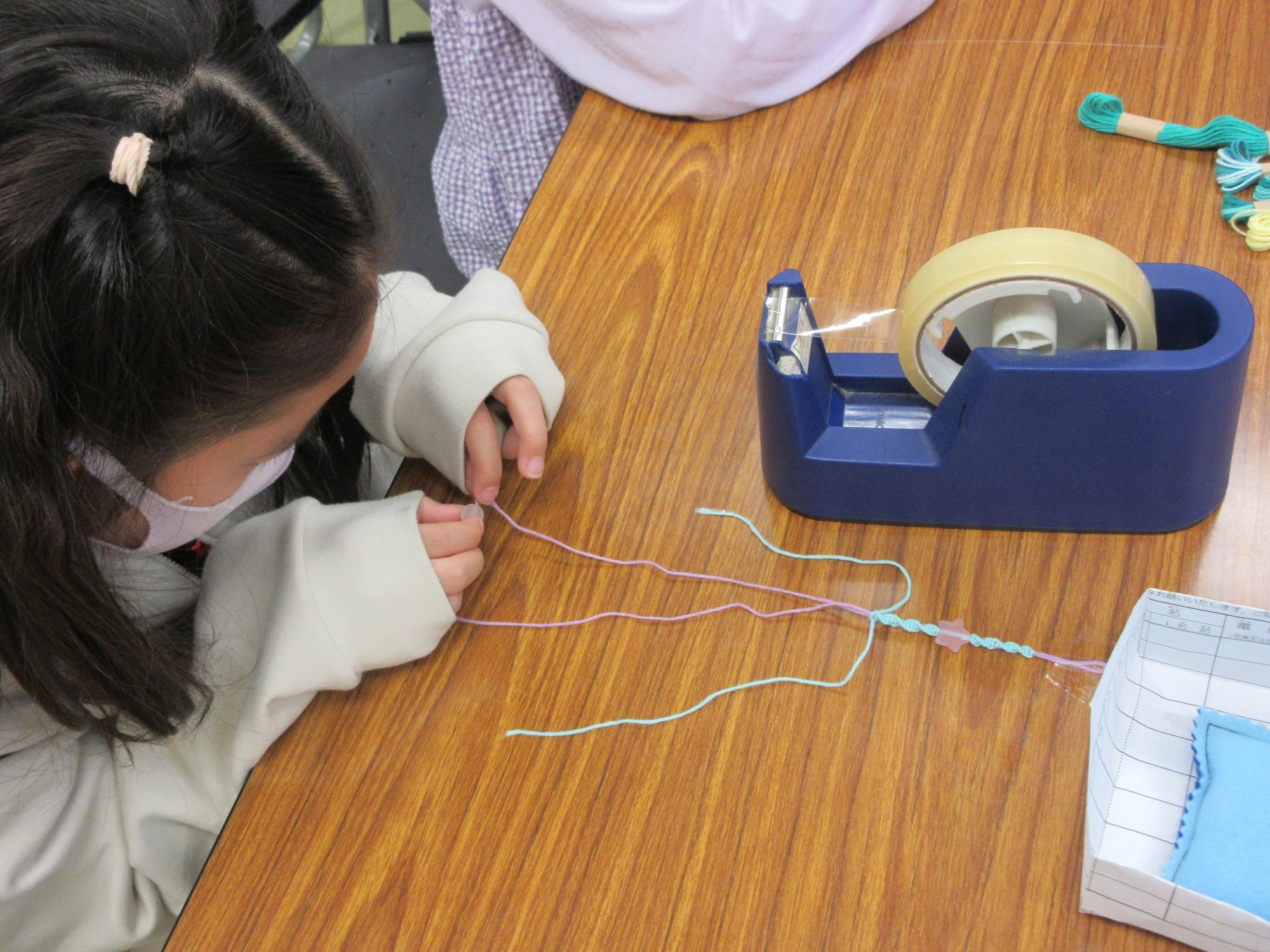 小学生が糸を編んでアクセサリーを作っている様子の写真