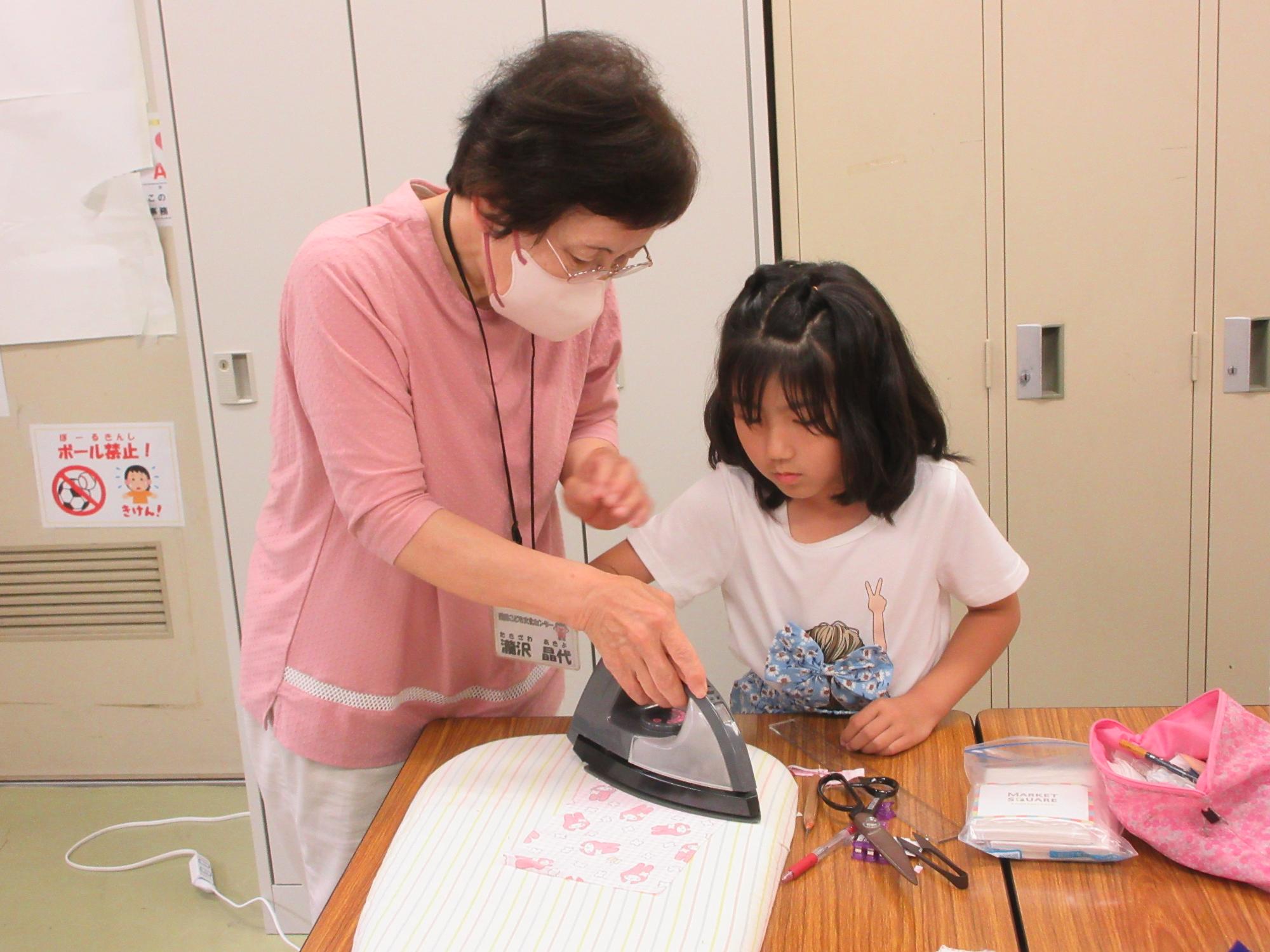 生地にアイロンをかける小学生と講師の様子