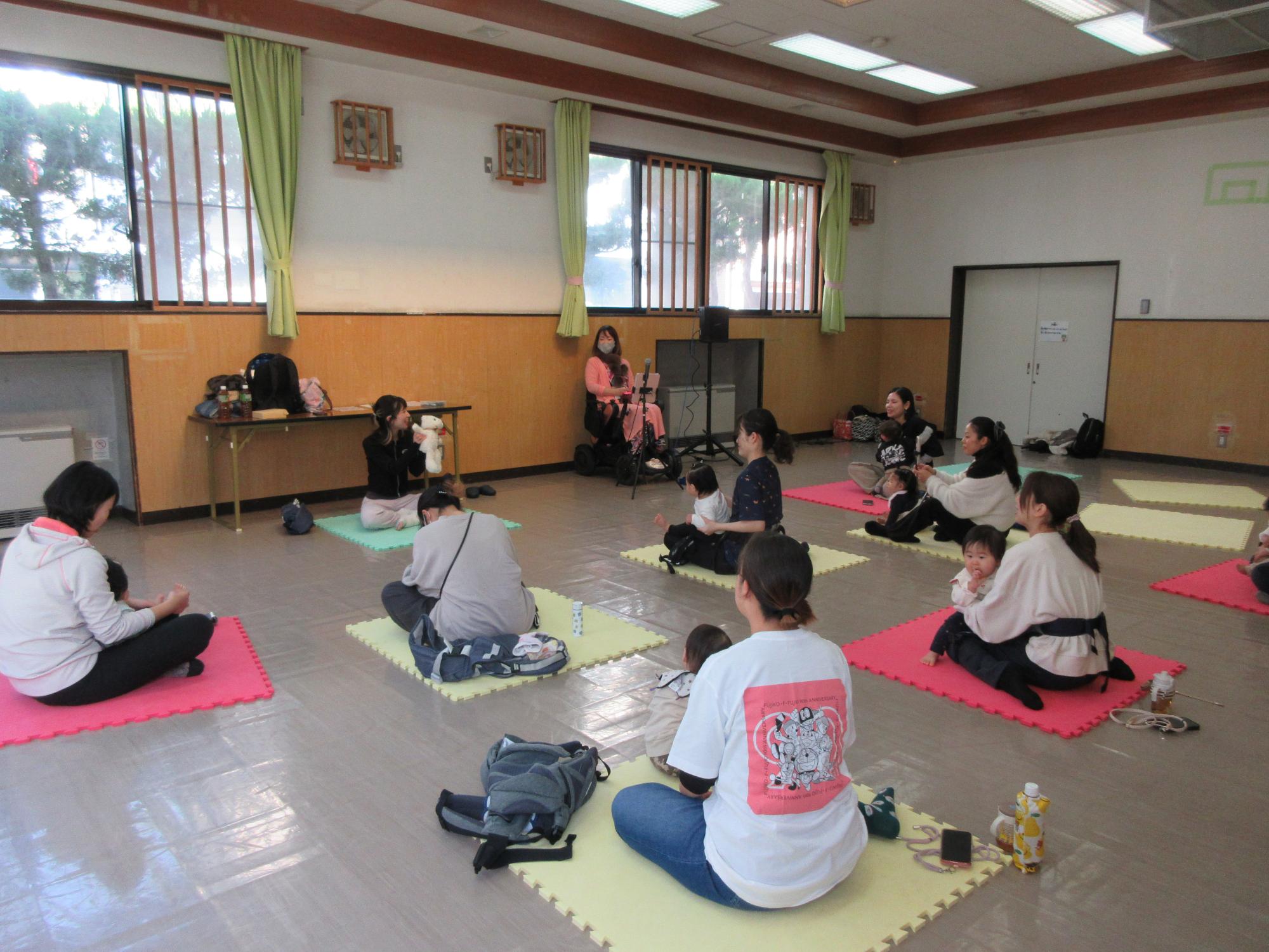 幼児親子がマットに座り、パペット人形を操る講師を見る様子