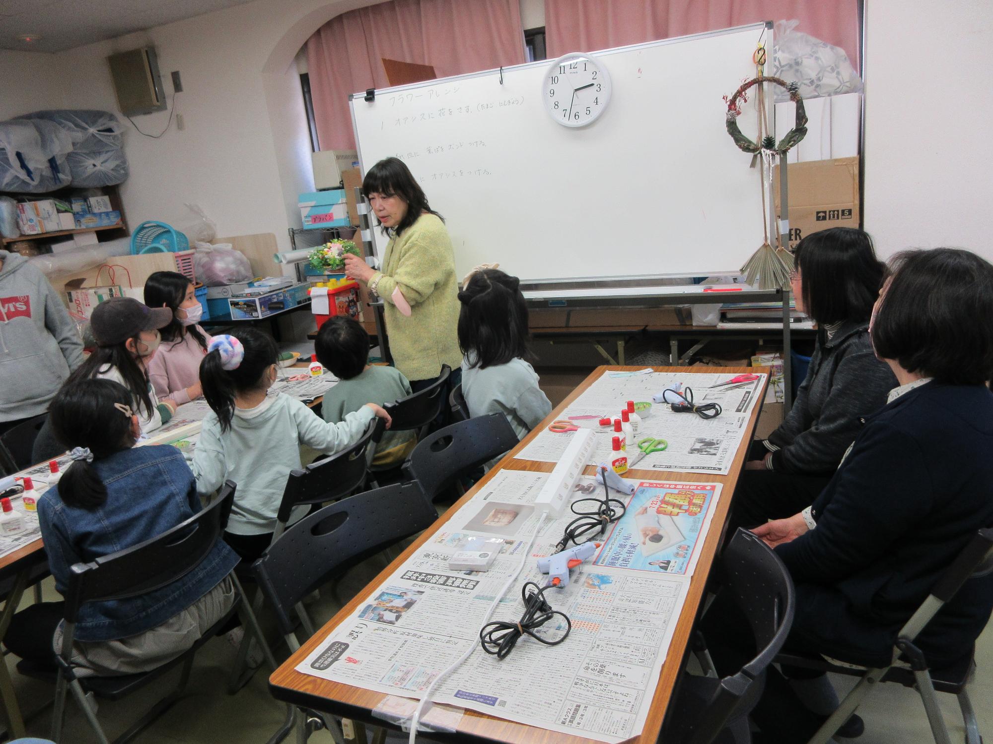児童たちがフラワーアレンジメントの説明を聞いている様子