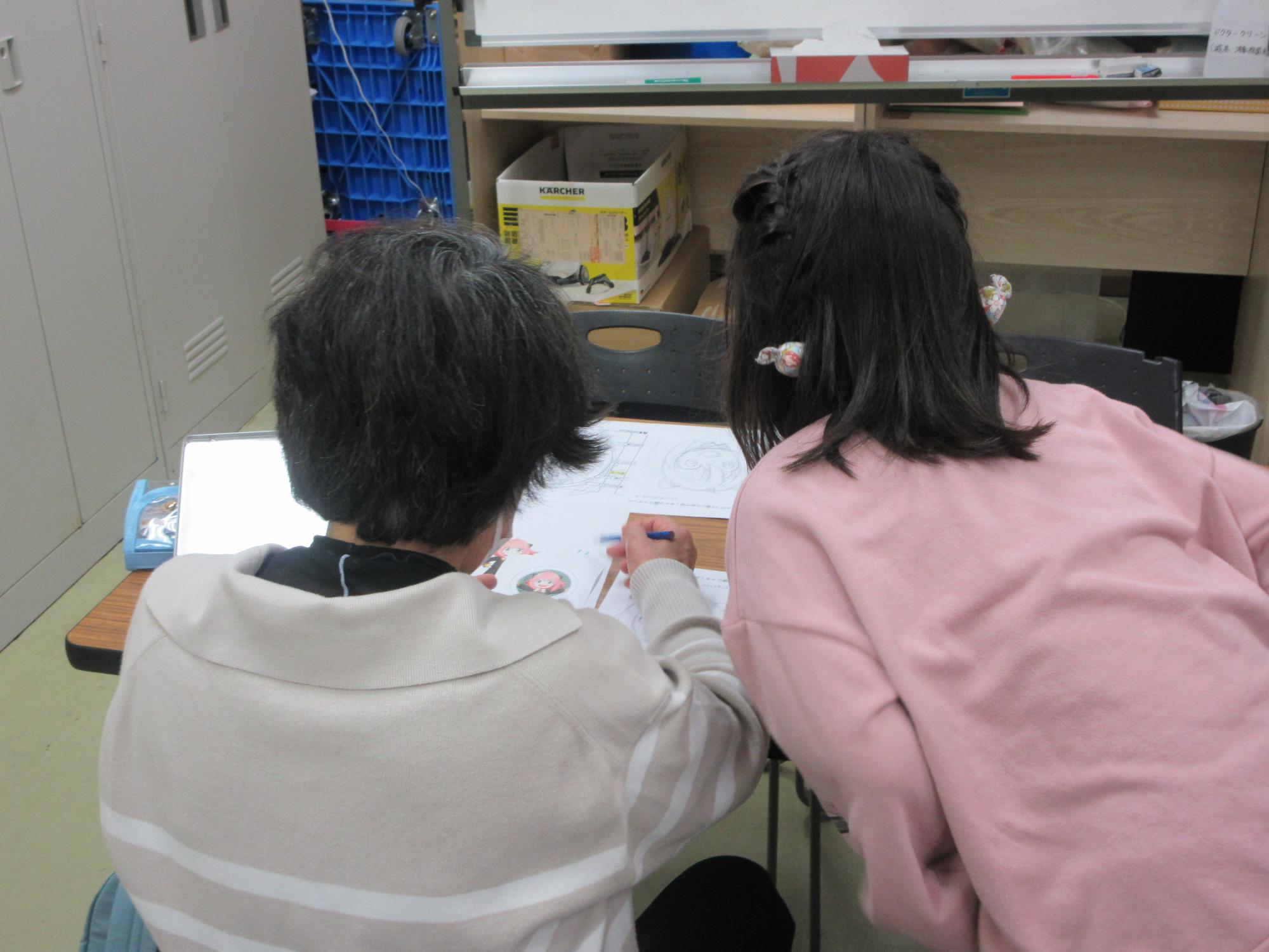 大人が絵を描いている様子を児童が覗いている写真