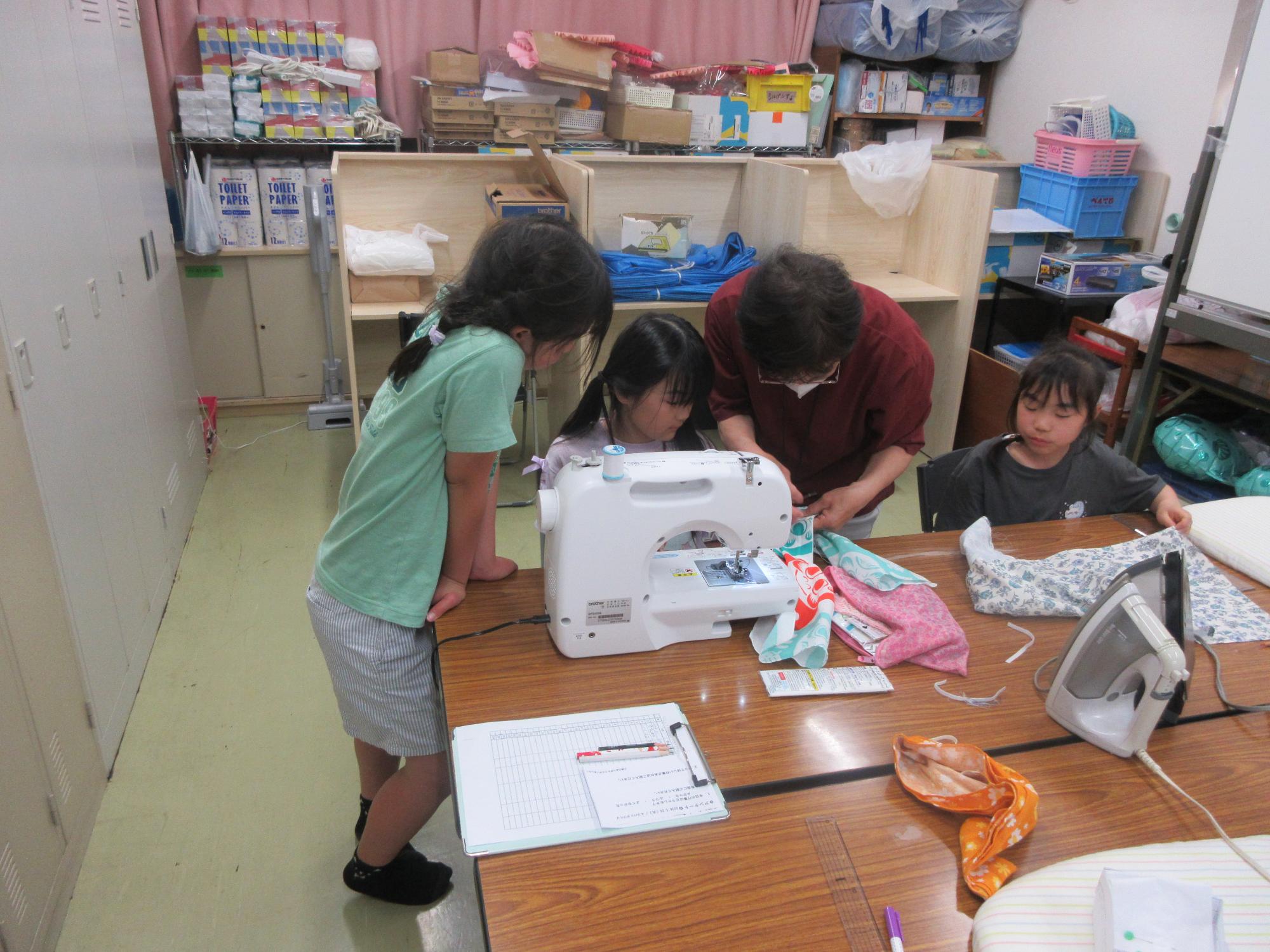 ミシンで生地を縫う小学生と補助をする講師の様子