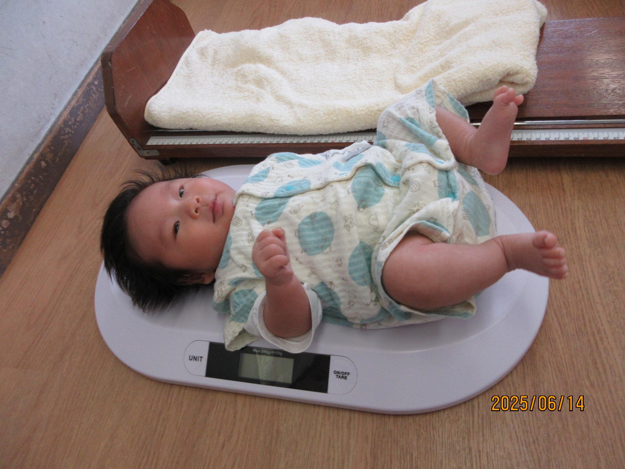 仰向けに寝転んだ乳幼児の身長をメジャーで測る2人のスタッフの写真