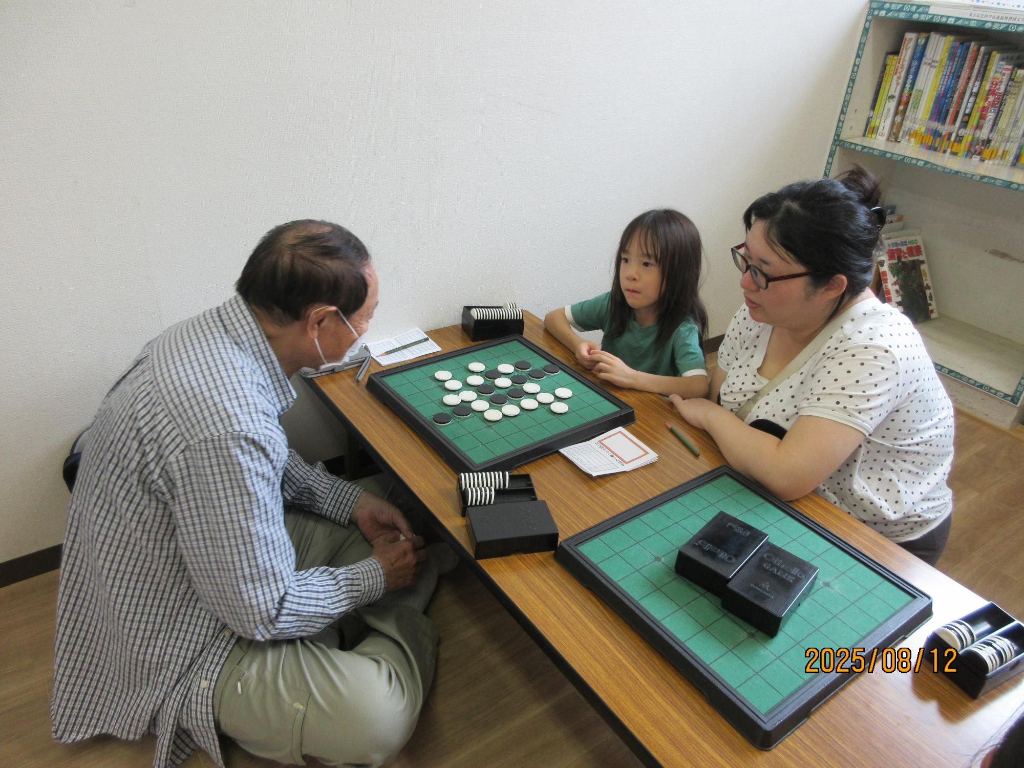 卓球台が置かれている室内で、床に広げたトーナメント表に記入をしている女の子と、その様子を周りで見ている児童達の写真