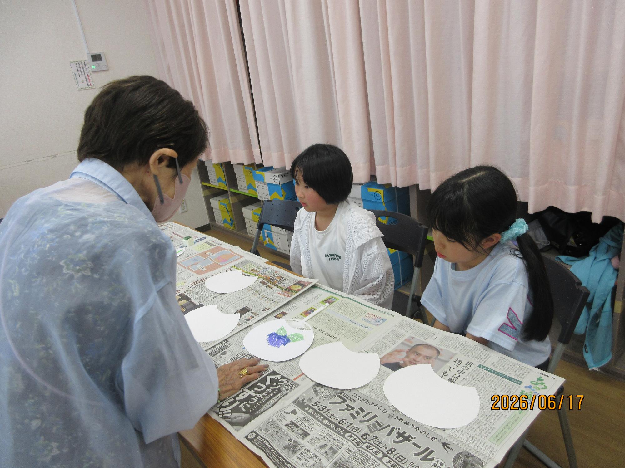 子どもたちが学習室で講師の先生から内輪の作り方をきいているところ