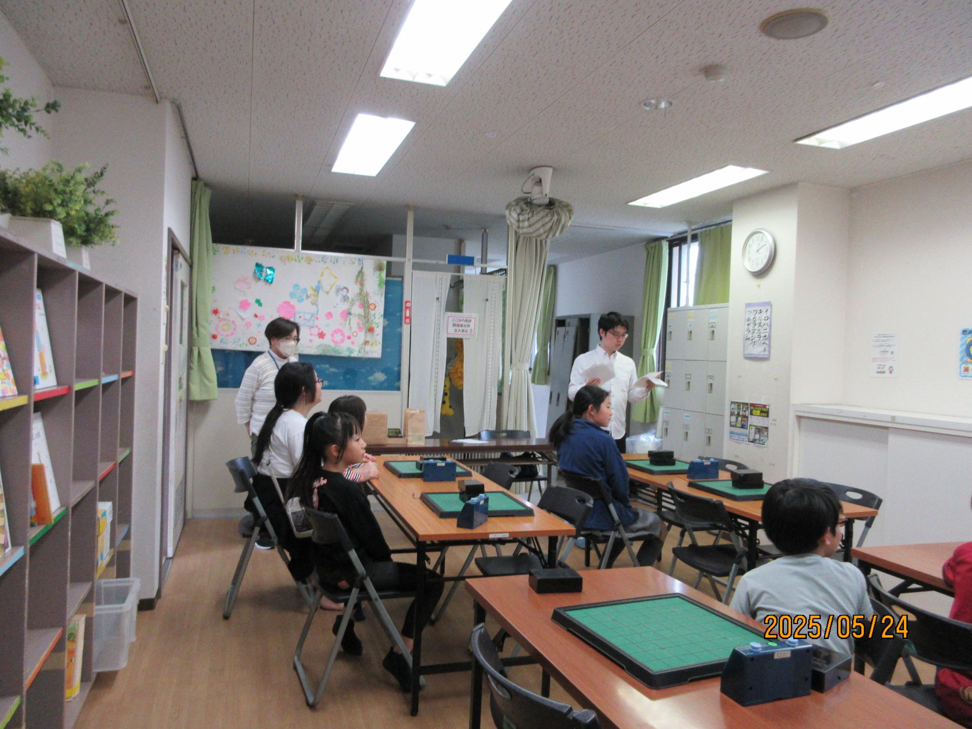 学習室でオセロ大会の説明を講師の先生がしているところの写真