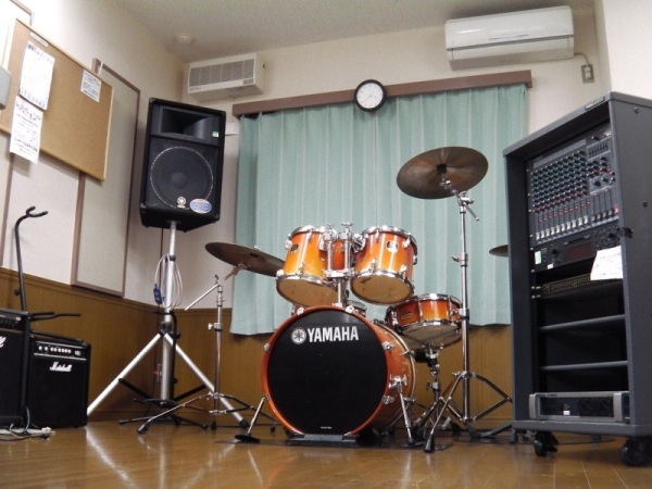 ドラムセットやスピーカー、アンプなどの機材が置かれた音楽室の写真