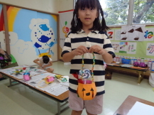 女の子が、紙で作ったカボチャのバッグを両手で持っている写真