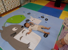 キャラクターの描かれたマットに寝転ぶ男の子を上から撮影している写真