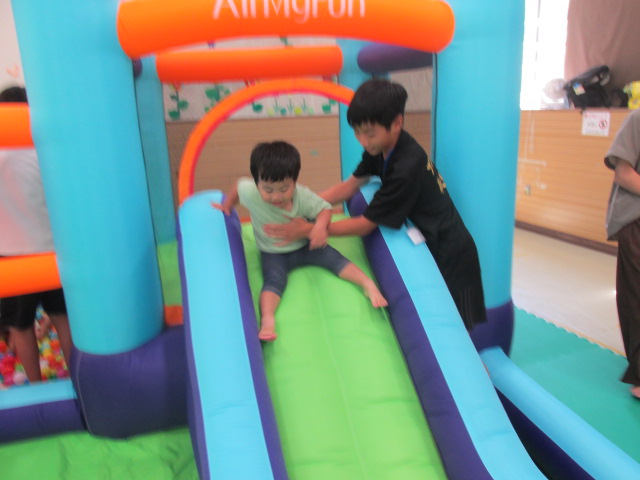 小学生ボランティアがすべり台の幼児を支えている写真