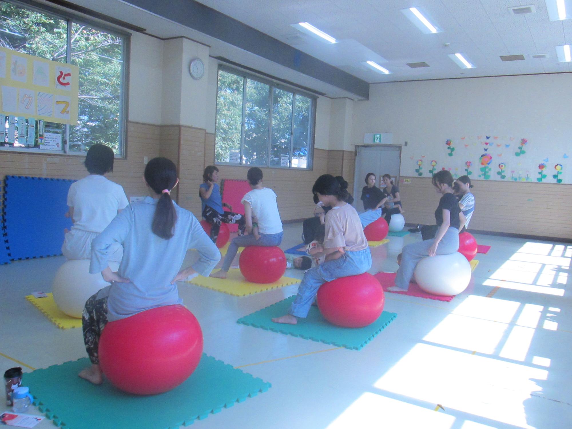 子どもを抱っこしながらバランスボールに座っている女性たちの写真