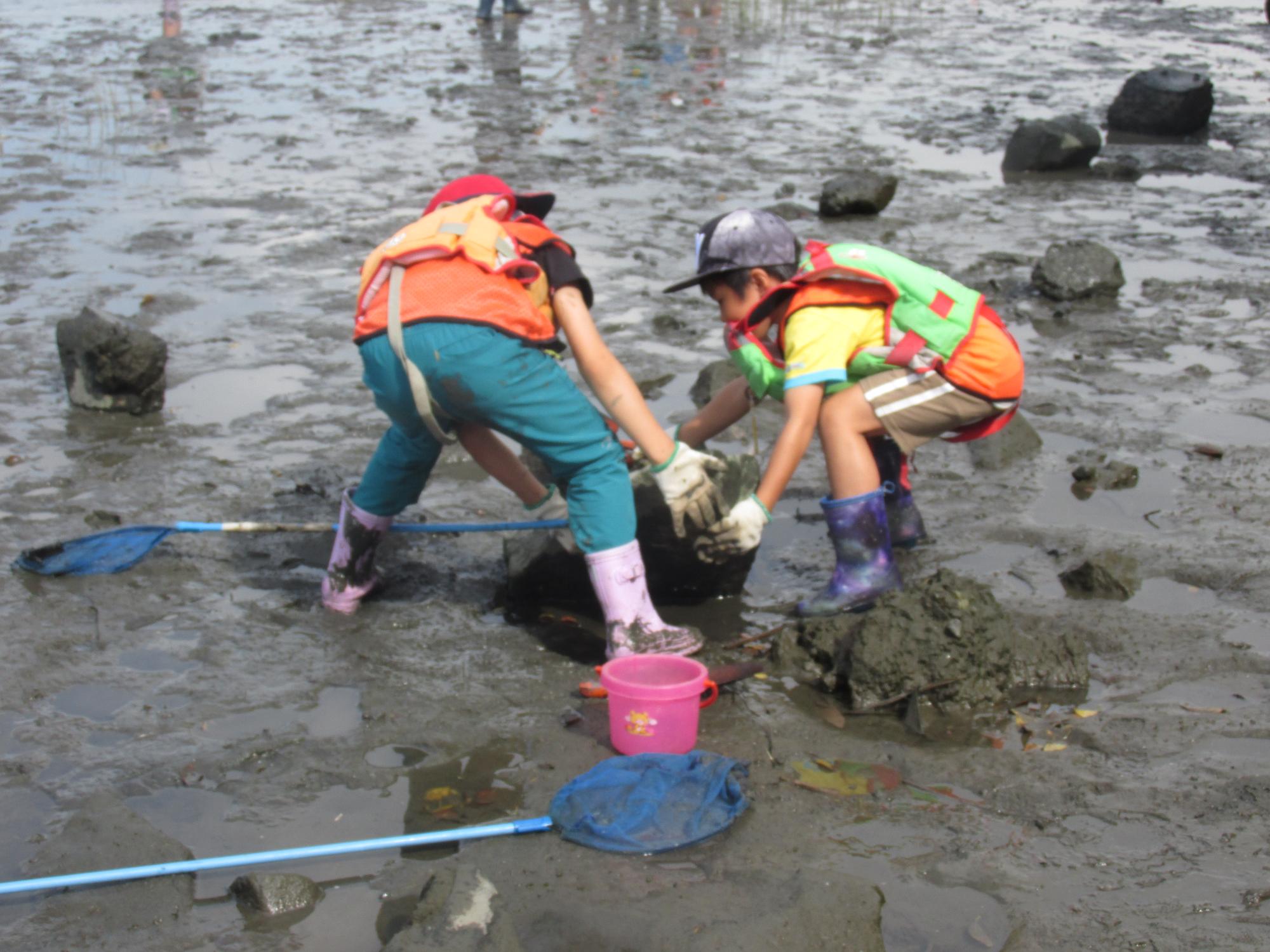 泥の中の大きな石を協力して動かしている子どもたちの写真