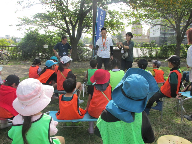 干潟でとれた生き物を説明するスタッフの話を聞いている子どもたちの写真
