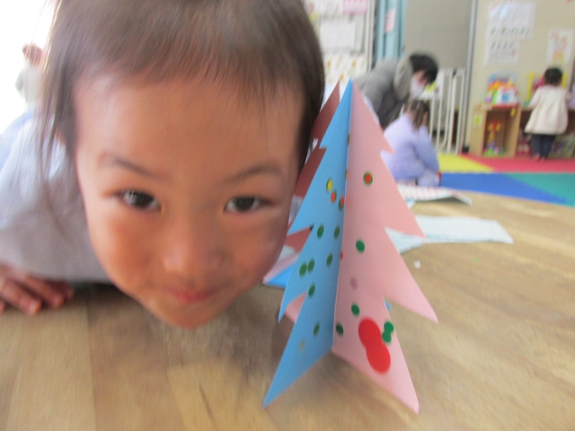 シール貼りしたツリーに顔を近づけている幼児の写真