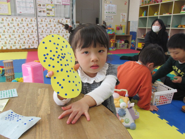 黄色いダルマに青のシールをたくさん貼った女の子の写真