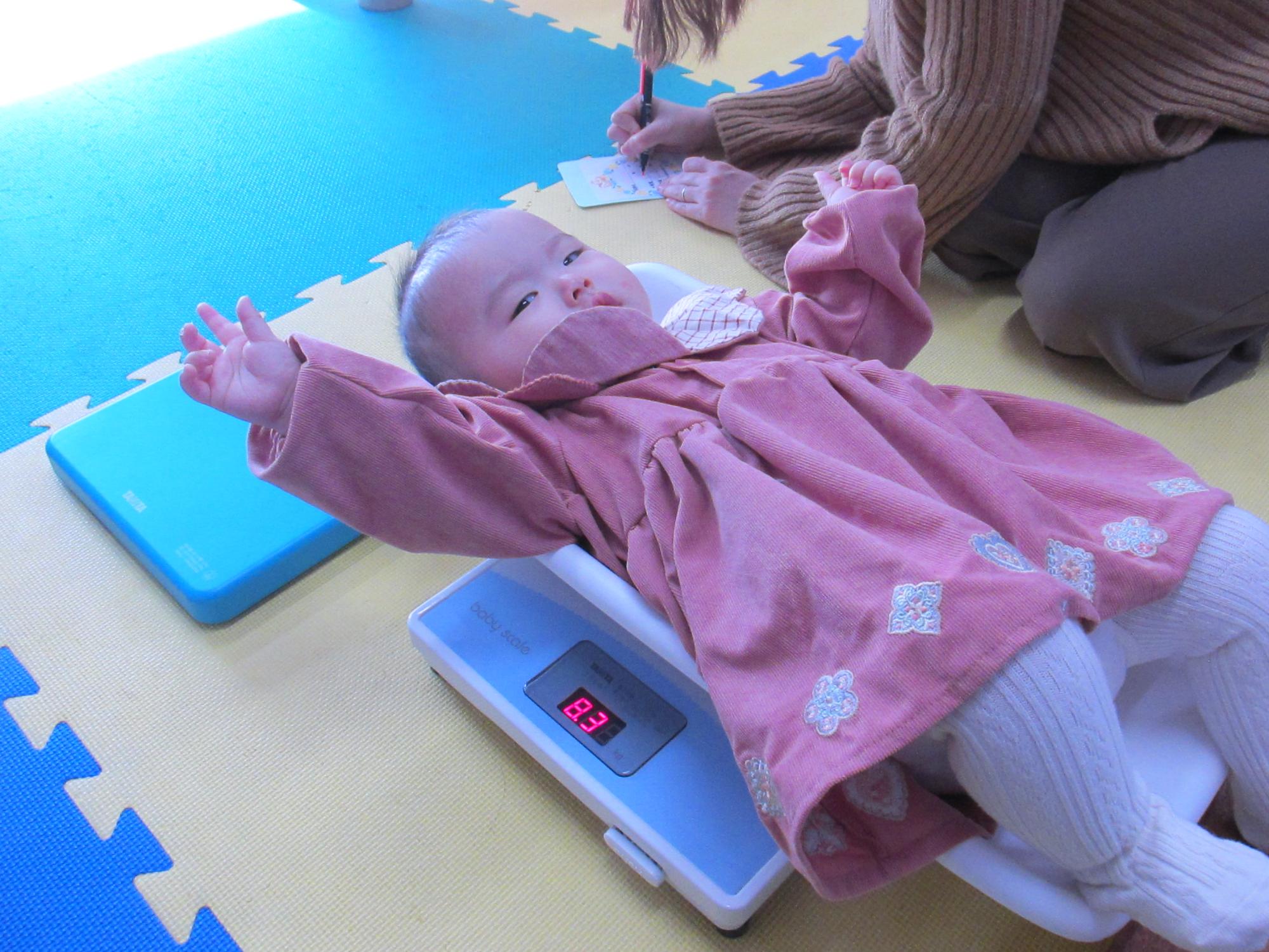 体重計に乗ってバンザイをしている幼児の写真