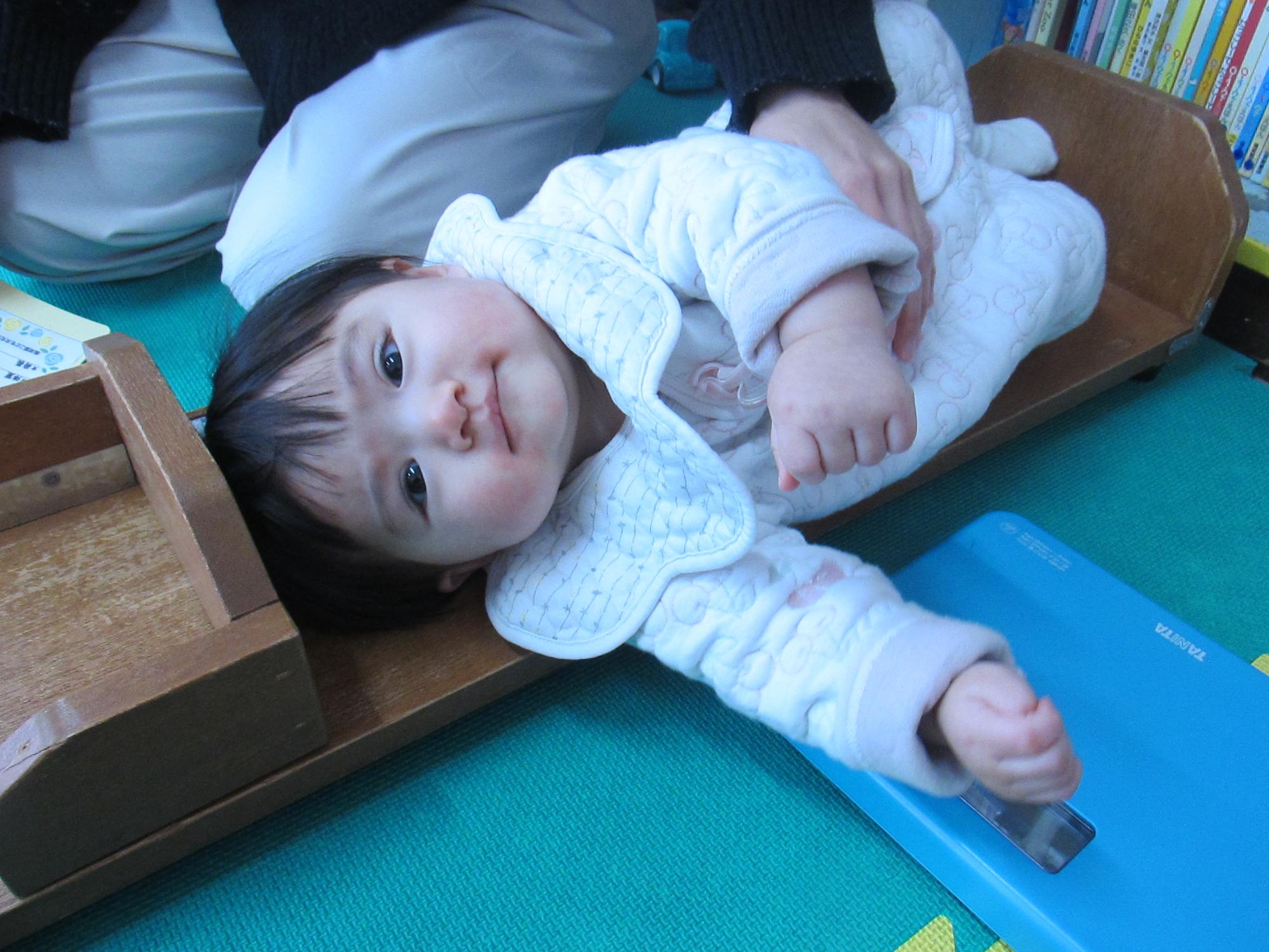 身長を測りながらこちらを向いてにっこりしている乳児の写真
