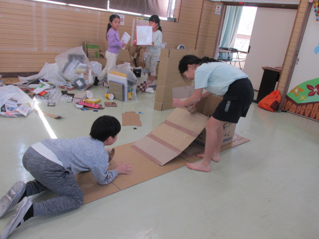 ジャンプ台のような坂からガムテープの芯を転がして遊んでいる子どもの写真