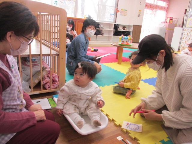 体重計に乗ってスタッフを見つめている幼児の写真