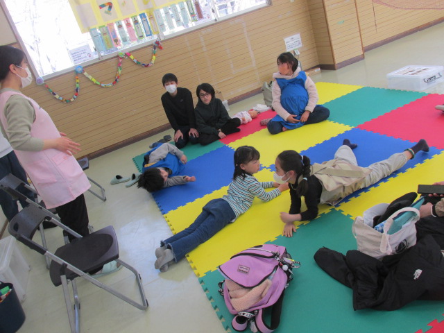 妊婦体験教材を身に着け座ったり寝転がったりしている子どもたちの写真