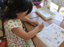 紙を片手で抑えながら真剣な表情で絵を描いている女の子の写真