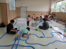 大きな施設内に張り巡らされたレールを広げていく参加者の子供と大人たちの写真