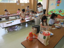 3つの長机の前に子供たちが座り持ってきた荷物を机の上にだしている写真