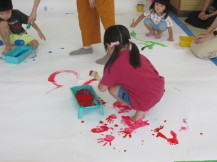ピンクの服を着た女の子が赤い絵の具を使い手や足型をとっている写真