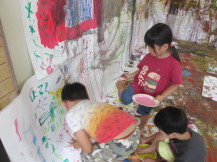 壁際の少し残った空間に男の子が落書きをしている様子を女の子が絵の具を片手にみている写真